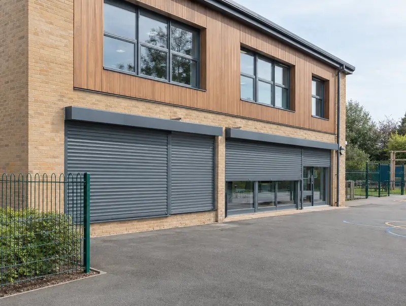 Grey roller shutters protecting the ground-floor glazing of a modern school